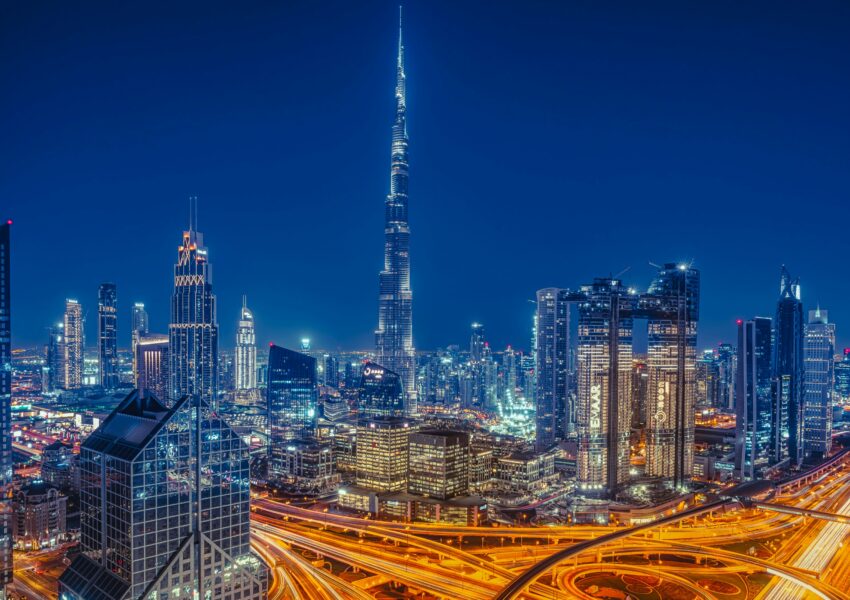 Night view of Dubai city skyline with Burj Khalifa, illuminated skyscrapers, and busy highways with flowing traffic lights.