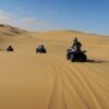 People riding off-road buggies across golden sand dunes during an exciting dune buggy tour Dubai, with clear skies and desert tracks visible.