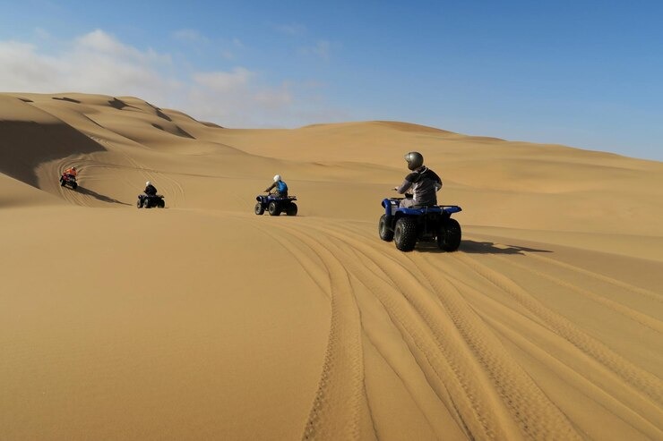 People riding off-road buggies across golden sand dunes during an exciting dune buggy tour Dubai, with clear skies and desert tracks visible.