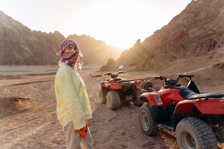Young traveler standing beside quad bikes during desert off road adventures, preparing for an ATV ride through rocky desert landscapes at sunset.