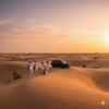 Private Desert Tours Dubai featuring a group of travelers standing on golden sand dunes at sunset beside a luxury 4x4 vehicle during an exclusive desert experience.
