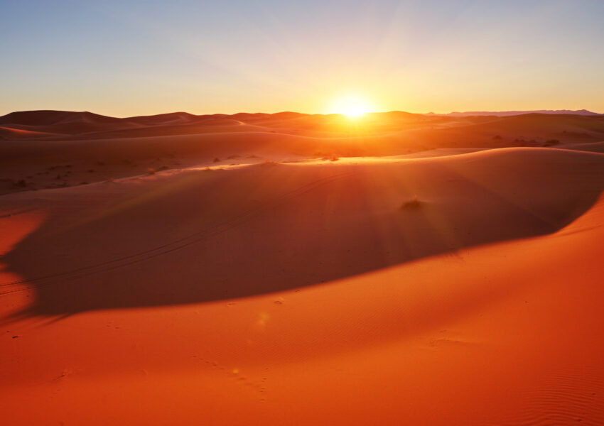 Golden sand dunes glowing at sunrise in a vast desert landscape, showcasing the serene beauty experienced on offbeat desert tours dubai.