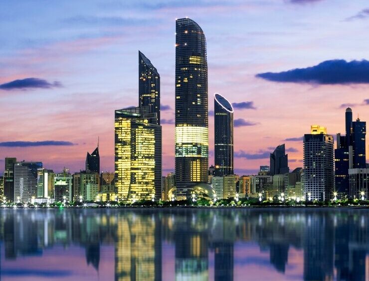 Abu Dhabi skyline at sunset reflected on calm water, showcasing modern skyscrapers during an Abu Dhabi private tour.