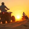 ATV Riding Dubai adventure with riders driving quad bikes across golden desert dunes at sunset