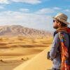 A traveler standing next to a 4x4 vehicle, gazing at vast golden dunes during a desert safari Abu Dhabi experience.