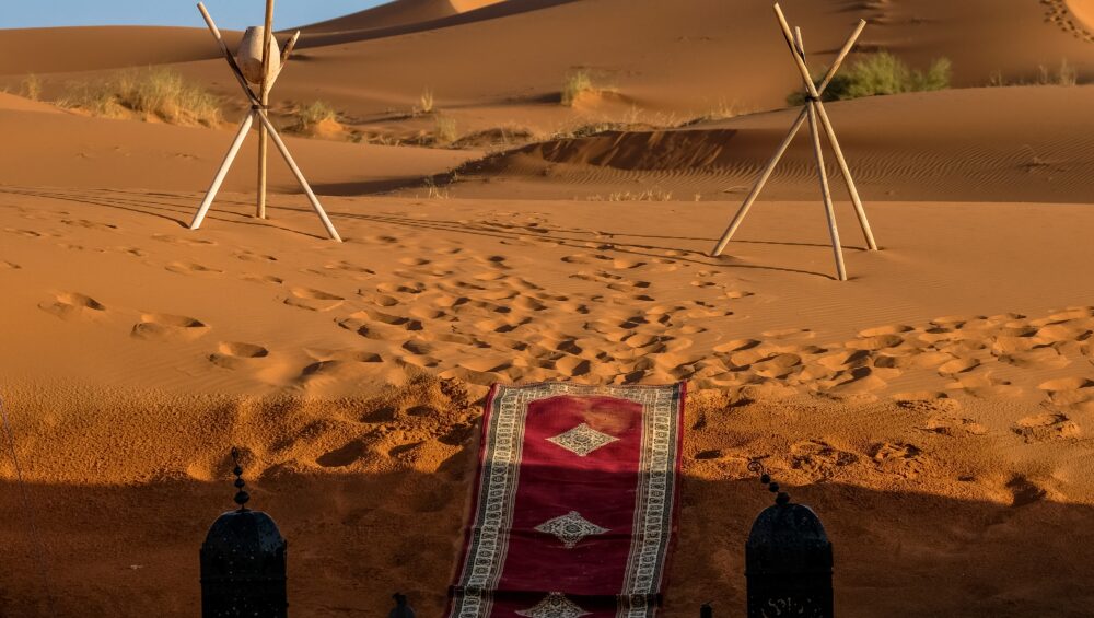 Red carpet walkway with traditional lanterns set among golden sand dunes, reflecting Bedouin Culture Dubai in a luxury desert camp setting.