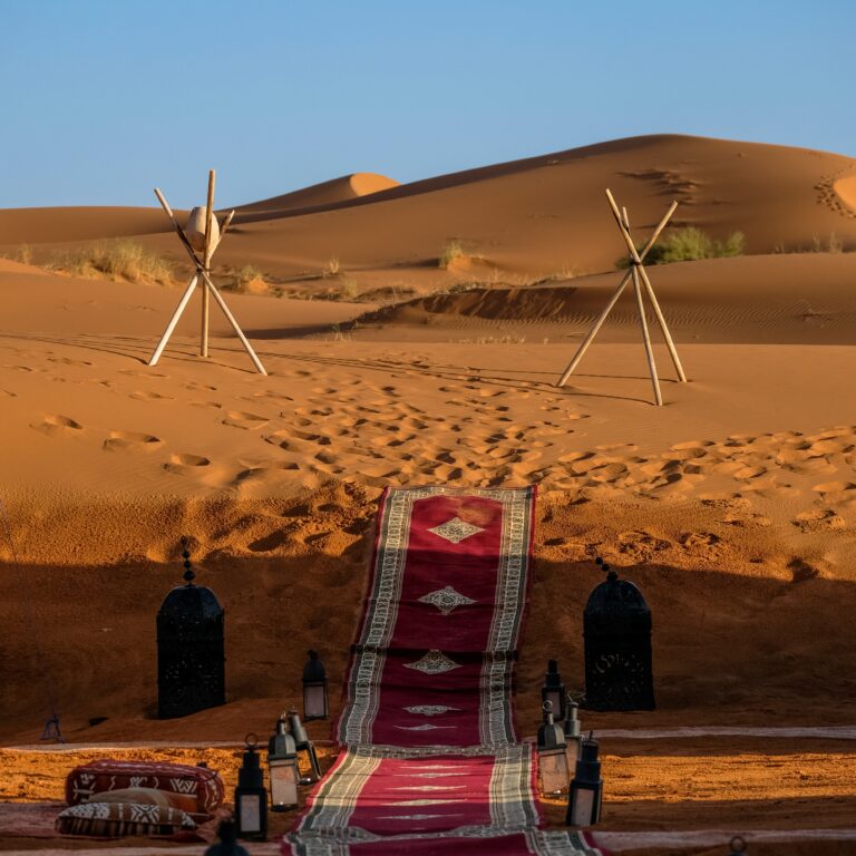 Red carpet walkway with traditional lanterns set among golden sand dunes, reflecting Bedouin Culture Dubai in a luxury desert camp setting.