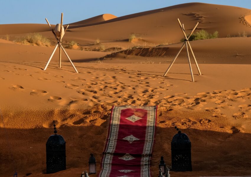 Red carpet walkway with traditional lanterns set among golden sand dunes, reflecting Bedouin Culture Dubai in a luxury desert camp setting.